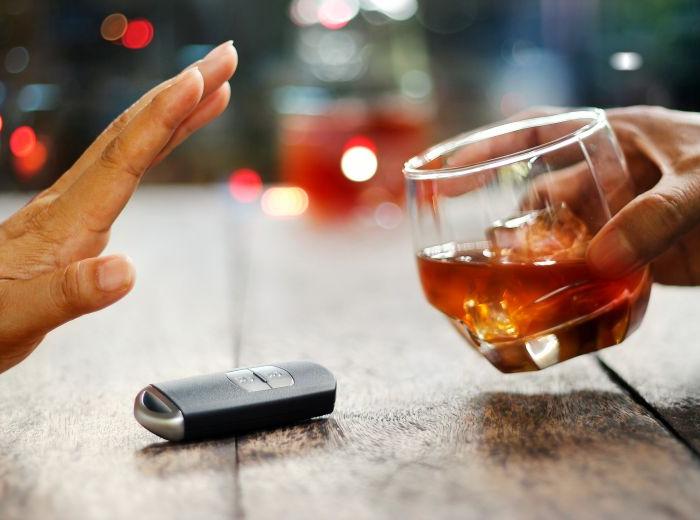 Main tendue pour refuser un verre d'alcool placé à côté d'une clé de voiture, illustrant le message de prévention contre la conduite en état d'ivresse.