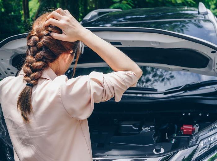 Femme de dos qui ouvre son capot de voiture pour vérifier le moteur 